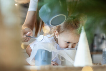 Mom and children decorate Christmas gingerbread at home. A boy and a girl paint with cornets with sugar icing on cookies. New Year's decor, branches of a Christmas tree.
