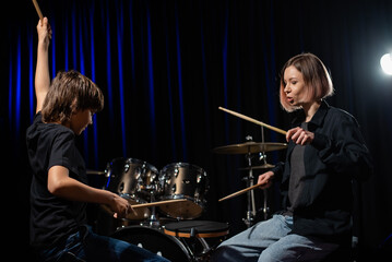 Fototapeta na wymiar Young caucasian woman teaches a boy to play the drums in the studio on a black background. Music school student