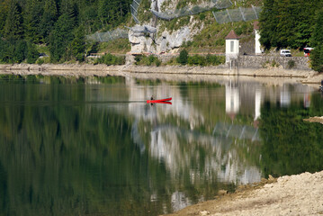 Fototapeta premium Fisherman in red canoe on a sunny late summer morning on Lake Klöntal. Photo taken September 4th, 2021, Klöntal, Switzerland.