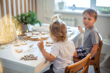Boy and girl decorate Christmas gingerbread at home. A boy and a girl paint with cornets with sugar...