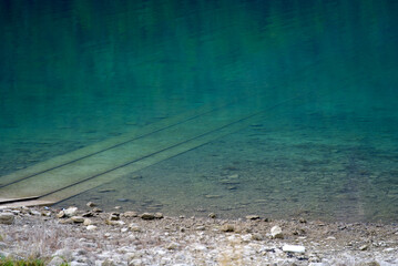 Railway tracks at Lake Klöntal at a beautiful late summer morning with reflections in calm water. Photo taken September 4th, 2021, Klöntal, Switzerland.