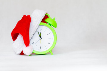 Alarm clock with Santa hat isolated on gray white background.Green clock with christmas red santa...