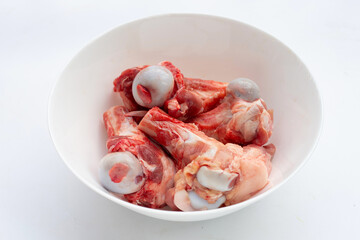 Raw pork bones in white bowl on white background.