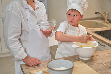 Mother and son cooking apple pie in the home kitchen. A woman and a boy in chef hats and aprons cook with pastries