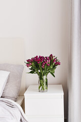 Alstroemeria flowers in a vase on a white bedside table. Simple and cozy bedroom decor. Minimal style. Fresh flowers in home decor and interior design