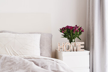 Naklejka premium Bedroom decor ideas. Minimal Scandinavian interior design. Fresh flowers and wooden decor on a bedside table. Simple and cozy room decor