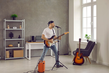 Middle aged man in bandana singing into microphone and playing on electric guitar plugged in AMP....