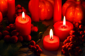 Candlelight in the dark. Halloween decor. Autumn orange pumpkins, red berries, dried oak leaves and three burning candles - 458672307