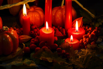 Autumn orange pumpkins, red berries, dried leaves and burning candles. Candlelight in the dark. Halloween Decor