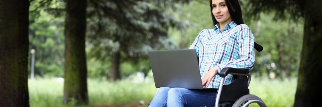 Young woman in wheelchair working on laptop in park