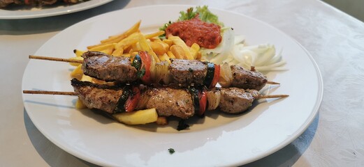 Pork skewers on wooden skewers with vegetables and fried potatoes