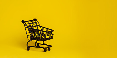 Black shopping cart isolated on a vibrant yellow background. Creative Black Friday concept. Sale or...