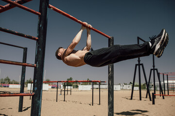young man doing abdominal exercise on horizontal bar in summer park. Workout element front lever - obrazy, fototapety, plakaty