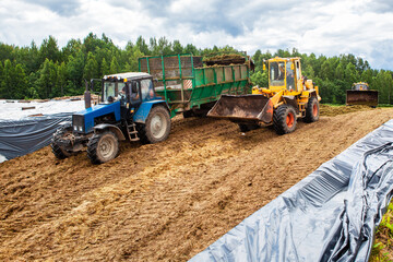A bulldozer and a tractor compact the cut grass in a silage trench.