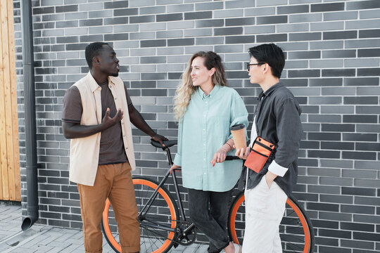 Modern African American guy and his female co-workers standing together outdoors talking about something during coffee break time