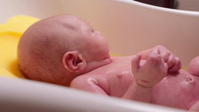Young mother bathes her newborn baby in a tub of warm water. An adorable boy takes a bath, his mother washes his willy in warm water. Concept is family, mother and son. 