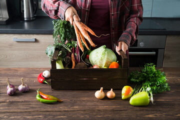 woman farmer in a linen apron with a box  of fresh garden vegetables in the kitchen. Organic Concept, clean eating
