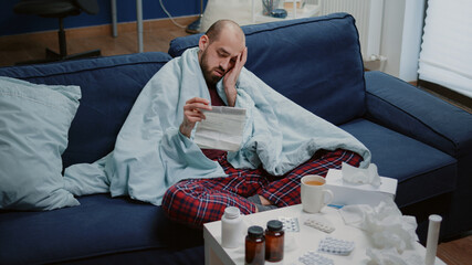 Man with sickness reading medicament information leaflet to heal cold and flu. Person with virus...