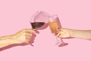 Celebrity concept. Two hands, man one holding glas of vine and gilr hand holding antique crystal glasses with lovely drinks in it against baby pink background
