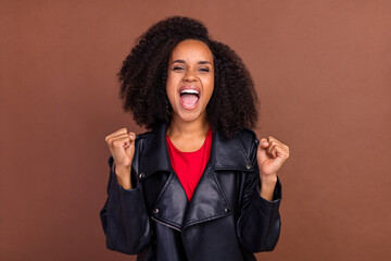 Portrait of delighted pretty carefree girl raise fists scream yes isolated on brown color background