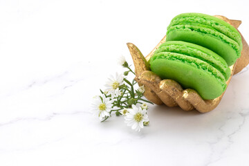 Two green macaroons on a gold wooden hand with tiny white flowers.