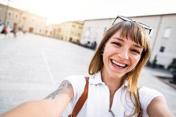 Naklejka premium Young woman take selfie with smart phone mobile walking on city street - Happy girl smiling at camera outside - People, technology, happy lifestyle and urban concept