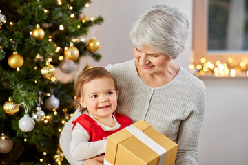 Obraz na płótnie Canvas christmas, holidays and family concept - happy grandmother and baby granddaughter with gift at home