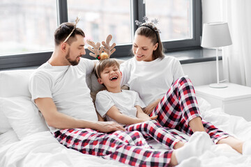 family, winter holidays and people concept - happy mother, father and little son in matching pajamas sitting in bed in christmas morning