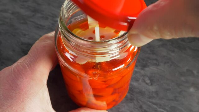 Closeup POV shot of a man’s hands removing the lid from a glass jar of mild red piquanté peppers in sweet and sour brine.
