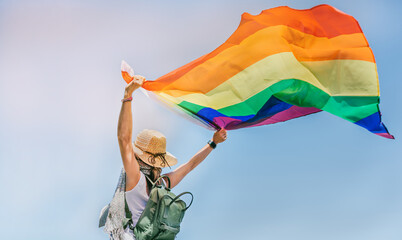 a woman wearing a hat holds a pride flag against a blue sky. concept of freedom and tolerance. lgtb