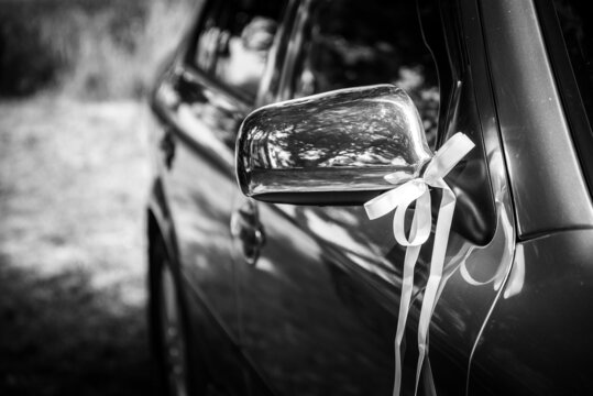 Mirror of wedding car decorated with ribbon. Black and white photo. Selective focus. Shallow DOF