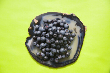 Flat lay of blue agate gemstone and juicy, fresh blueberries on green table. Isolated sweet bilberry fruits on translucent crystal surface on white background. Copy Space. Healthy raw vegetarian food 
