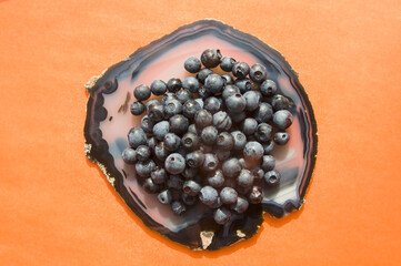 Flat lay of blue agate gemstone and juicy fresh blueberries on orange table. Isolated sweet bilberry fruits on translucent crystal surface on white background. Copy Space. Healthy raw vegetarian food 