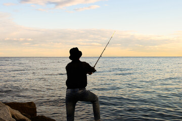 Silhouette of a caucasian boy fishing on the sea.