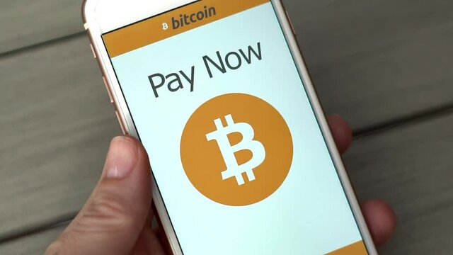 Pay online with Bitcoin concept footage in slow motion. Person uses smart phone to pay for goods online using cryto currency bitcoin. Grey table in background, natural light in slow motion
