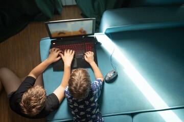 two boys playing on laptop on sofa © avtk