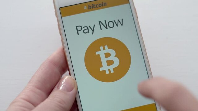 Pay online with Bitcoin concept footage in slow motion. Person uses smart phone to pay for goods online using cryto currency bitcoin. White background, natural light in slow motion
