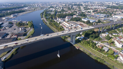 Fototapeta premium CAEN, FRANCE-SEPTEMBER 2021: Viaduc de Calix on the canal de caen. The largest bridge in Caen, an important road E46 for cars. A photo from the drone, in the phone is buildings and greenery