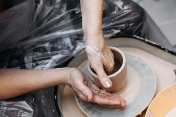 Woman hands forming clay cup spinning on pottery wheel on pottery workshop