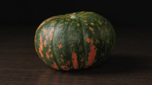 A green-orange pumpkin is lying on the table. Autumn is the time of harvest. A ripe vegetable on a black background.