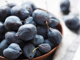 Large autumn blue plums lie in a natural clay bowl. Natural fruits from the garden.