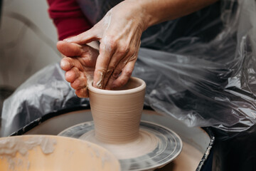 Fototapeta na wymiar Potter hands forming clay cup spinning on pottery wheel on pottery workshop