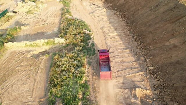 Dump truck drives to load sand on a dusty road in the open pit. Tipper truck working in quarry. Drone view of the opencast mine. Sand and gravel is excavated from earth. Construction site.