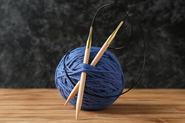 Yarn ball with knitting needles on wooden table