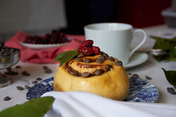 cinnamon roll in blue earthenware plate with chocolate chips and blueberries on white tablecloth