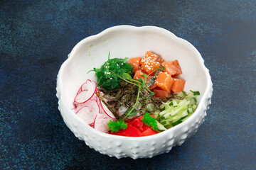Poke with salmon, radishes and cucumbers in a plate. Against a dark background.