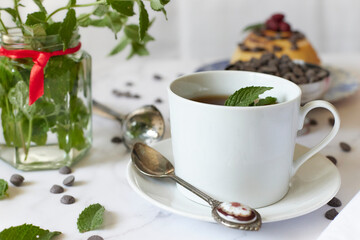 Tea in white earthenware mug with mint leaves on white tablecloth