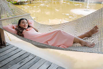 happy Asian woman lying down relax on betting hammock near water pond. summer vacation.