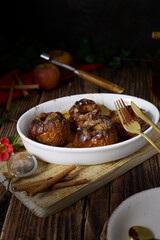 roasted red apples with cinnamon and honey in white earthenware dish on dark wooden table