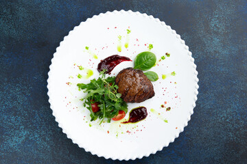 Beef medallions with arugula and tomatoes in a plate. Against a dark background.